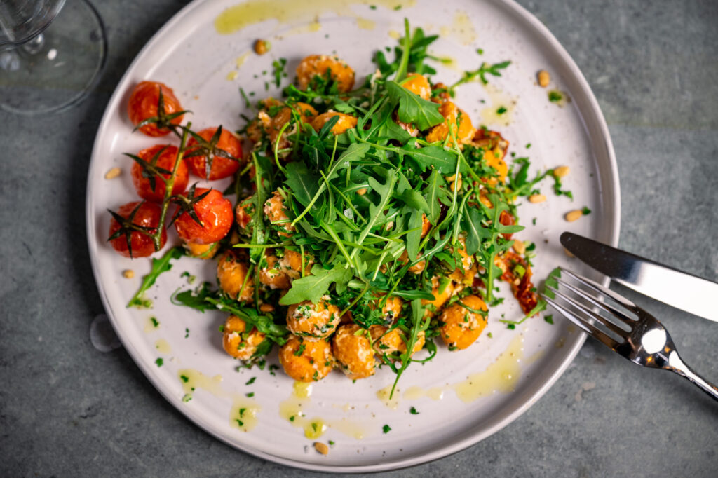 Schön angerichteter Teller mit Süßkartoffelgnocchis, Ruccola und kandierten Tomaten