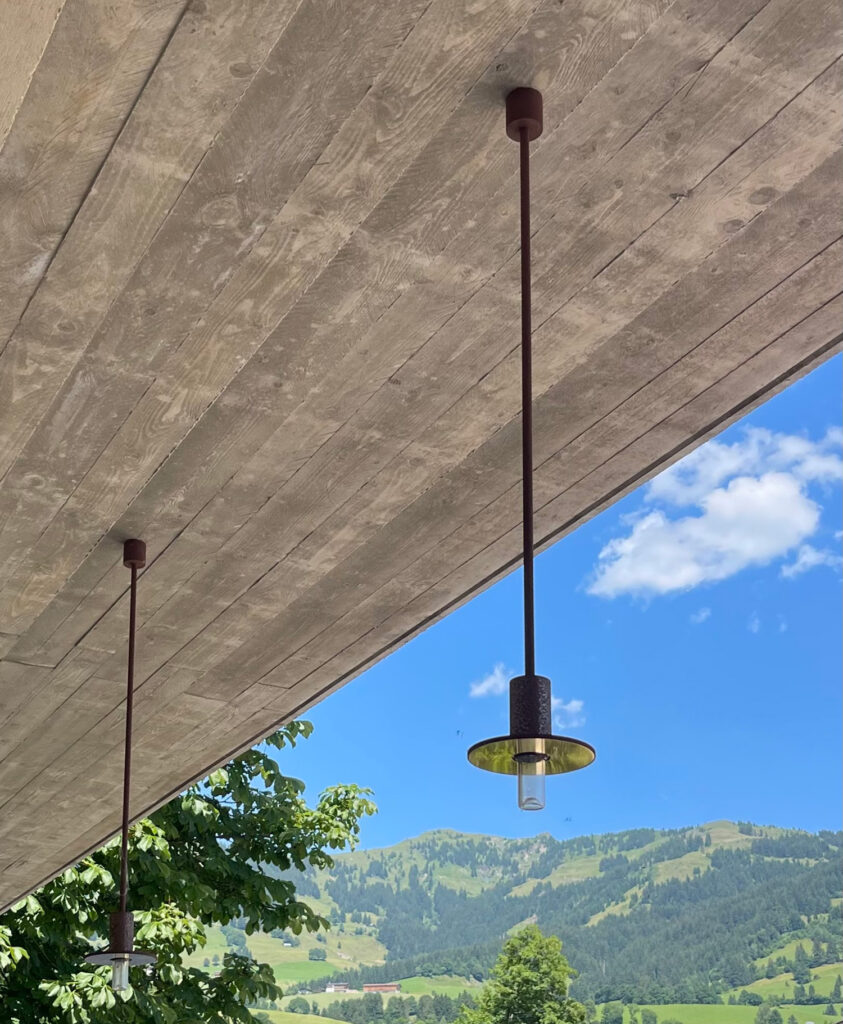 Im Hintergrund ein wunderschöner Ausblick auf die Berge. Im Vordergrund das Abdach mit Hängelampen des Gasthauses.